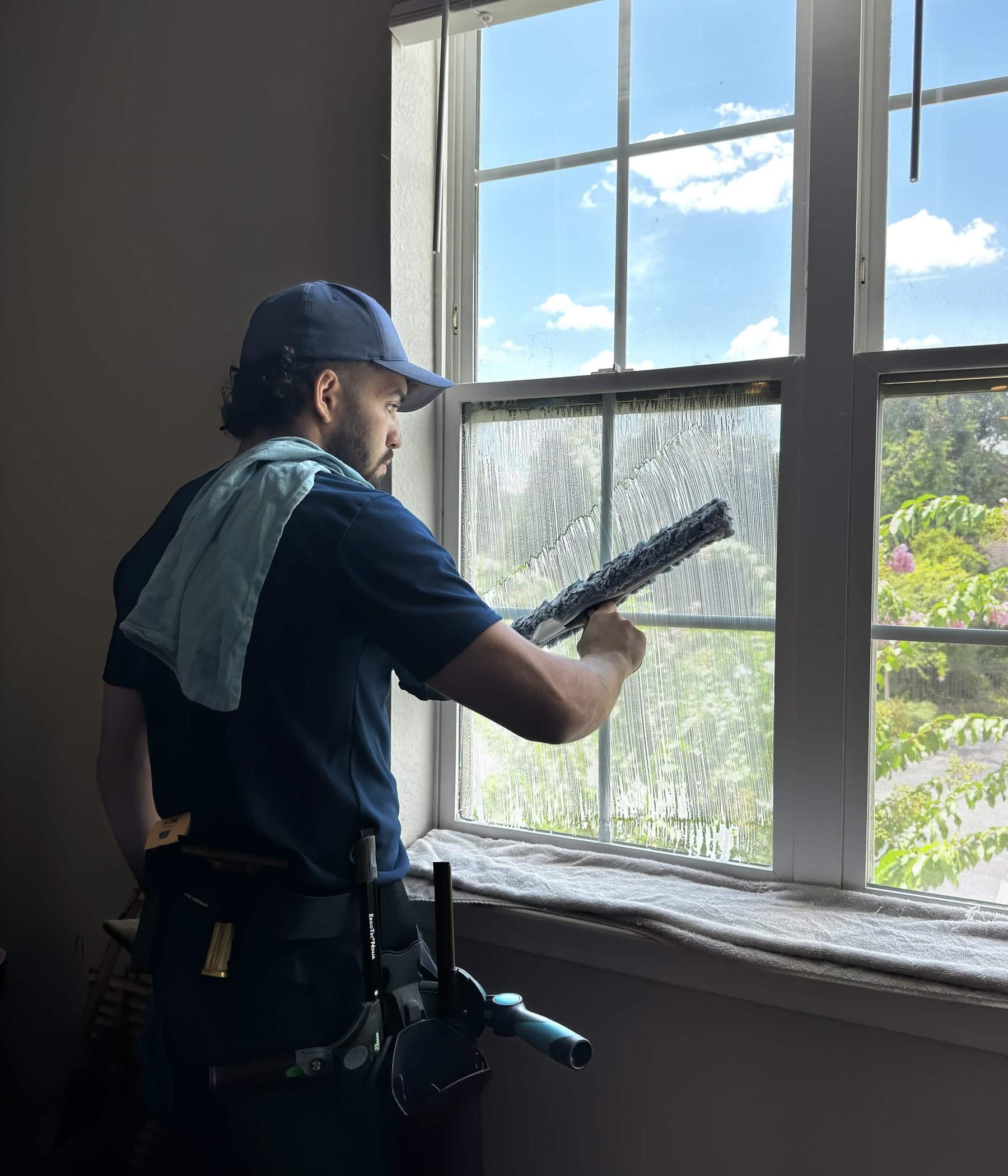 CrestFlow technician squeegeeing a tall interior window with sunlight coming through the glass