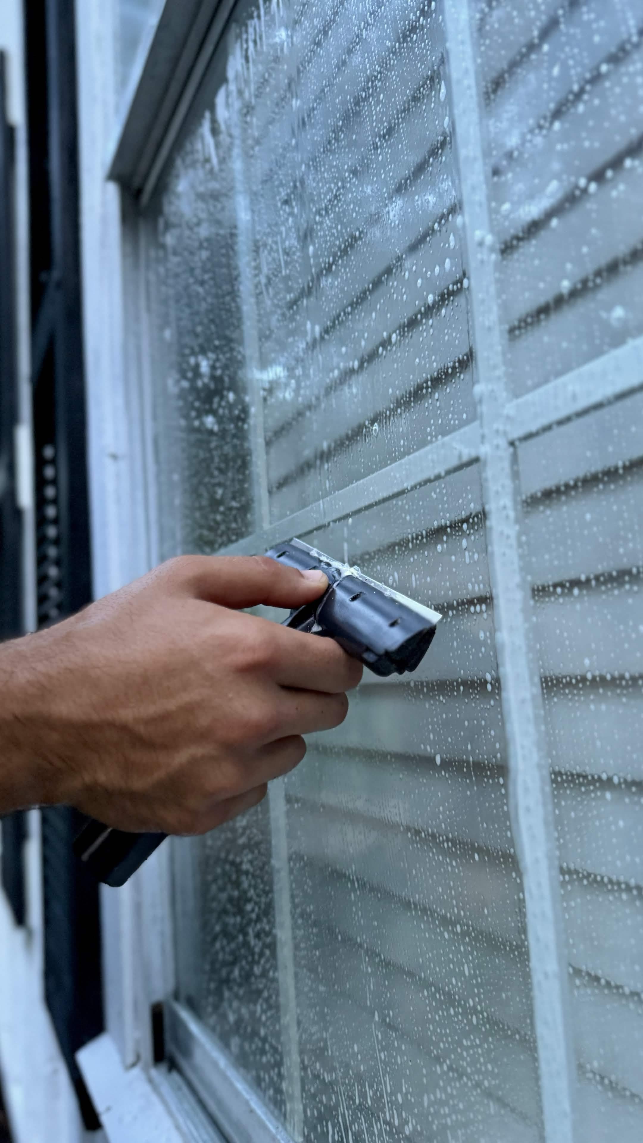 Close-up of a squeegee pulling soap and hard water film off a pane of glass