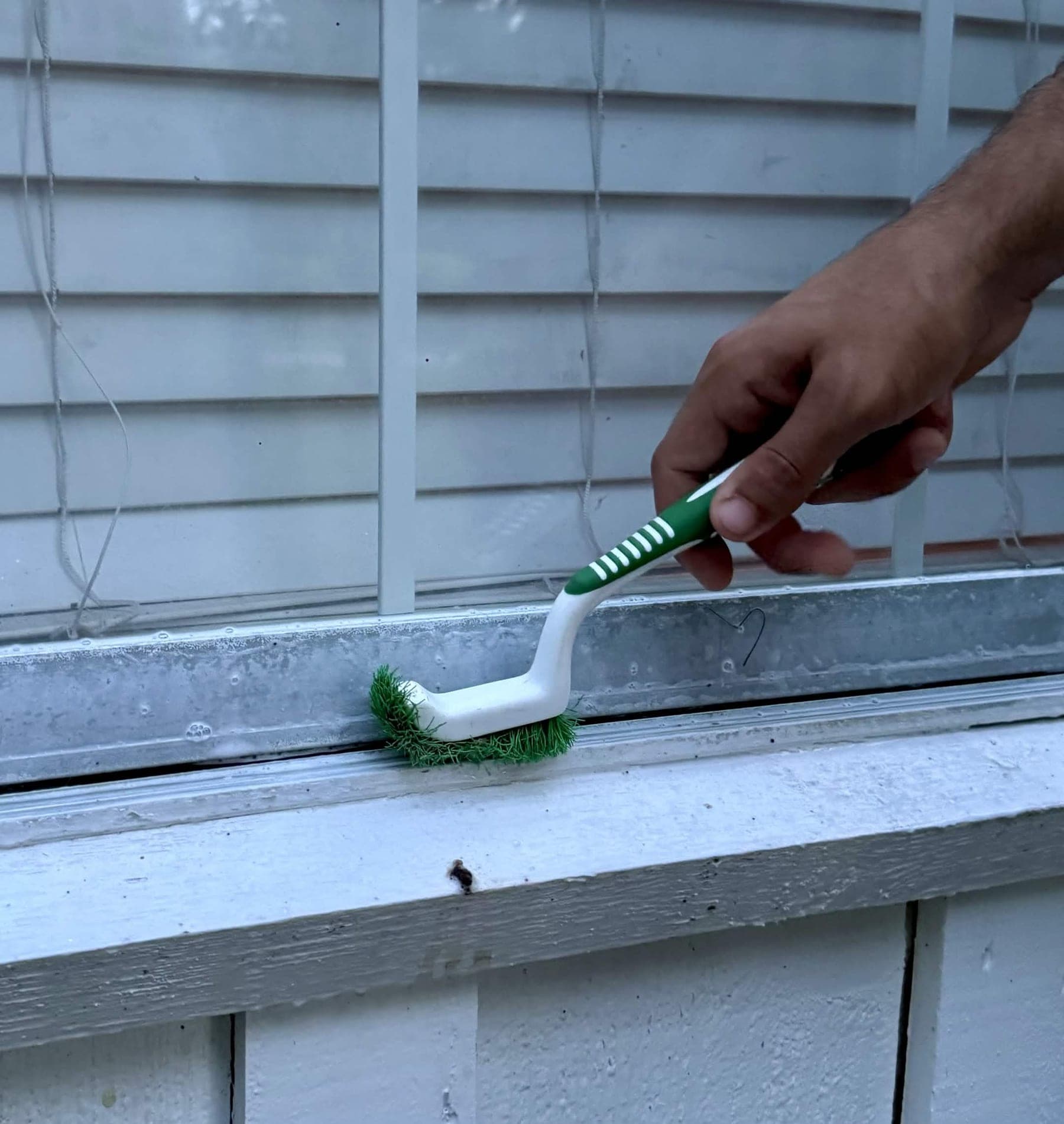 Detail brush scrubbing packed dirt out of an aluminum window track